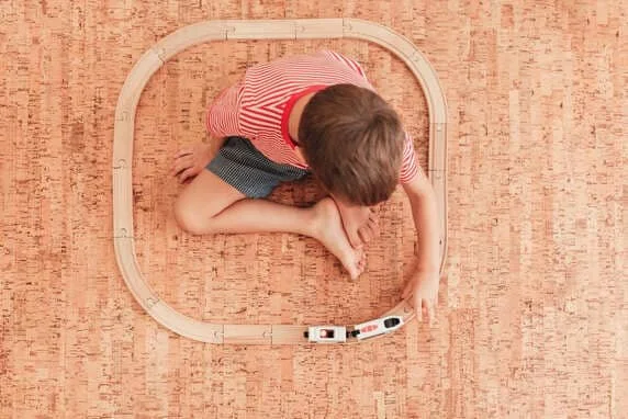 Kind spielt mit Holzeisenbahn auf einem Korkboden